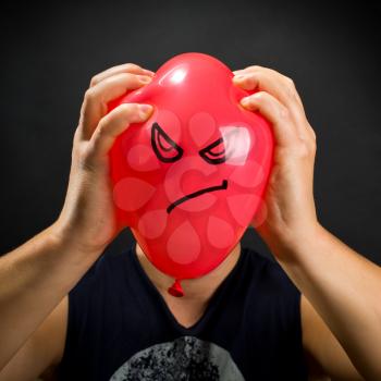 Man squeezing red balloon with angry smiley