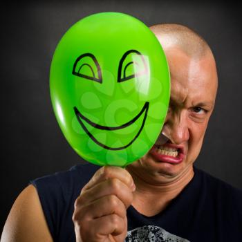 Angry man hiding behind green balloon with happy smiley