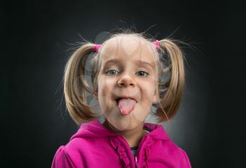 Beautiful little girl showing her tongue on gray background