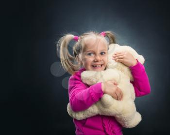 Small cute girl holds toy bear on grey background