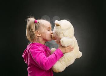 Little cute girl kisses toy bear on grey