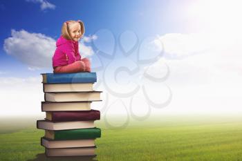 Small girl sits on the pile of books on nature background