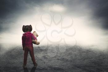 Little girl standing back with toy bear in the darkness