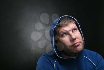Adult man in the hood sits thinking on dark background