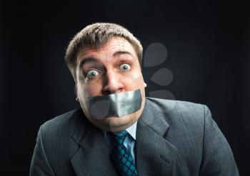 Surprised man with mouth covered by masking tape preventing speech, studio shoot
