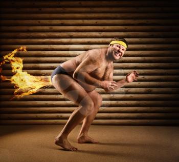 Very strange naked man farts by fire on the background of wooden wall