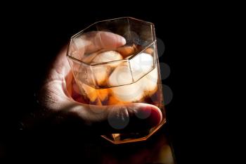 Gold whiskey on the rocks in alcoholic's hand