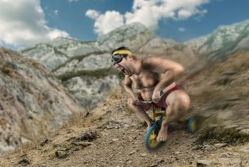 Adult naked man cycling in the mountain on child's bicycle