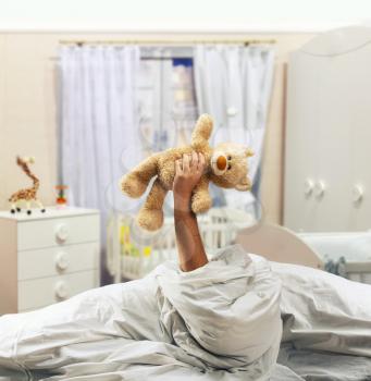 Hand holds toy bear above the bed in home interior