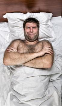 Top view of unhappy man with crossed hands in white bed