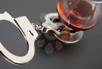 Close-up of handcuffs lock with glass of alcohol on background