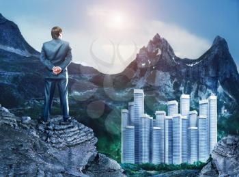 Businessman standing back on the cliff looking at the city