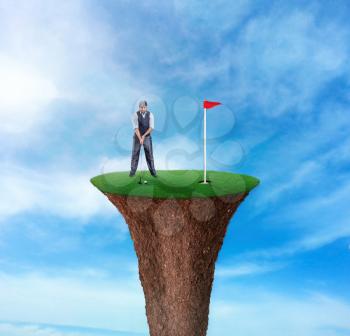 Businessman playing golf on the top of a grass cliff