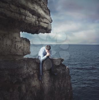 Frustrated businessman sits on edge of the cliff near the sea