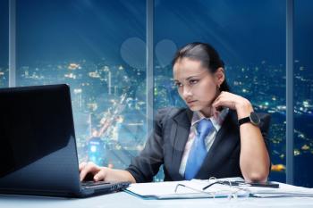 Businesswoman working in office against night cityscape