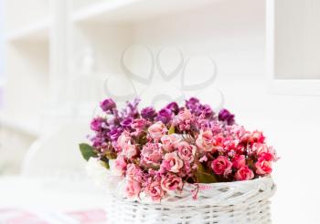 Beautiful bouquet of bright flowers in basket on white table