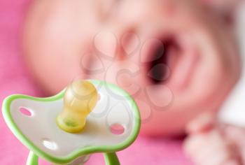 Close-up of pacifier with crying baby on background