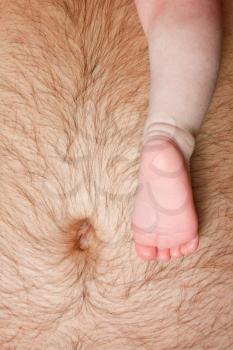 Close-up of newborn baby leg on father's abdomen