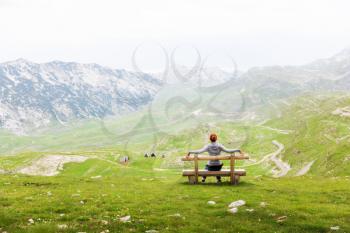 Girl is sitting on wooden bench in mountain landscape. National Park Durmitor, Montenegro, Europe