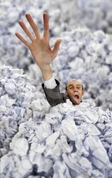 Businessman sinking in big heap of crumpled papers and asking for help