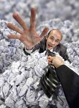 Helping hand saving businessman buried in big heap of crumpled papers