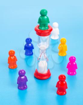 Time is money concept. Colorful toy people standing in a circle around sandclock