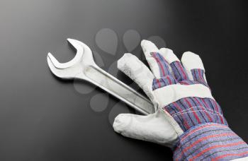 Stainless steel wrench and work glove on grey background