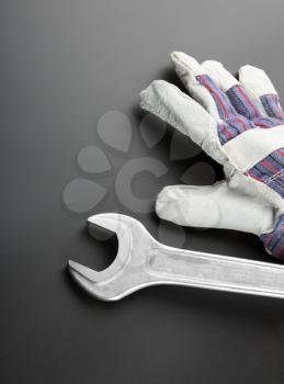 Stainless steel spanner and work glove on grey background
