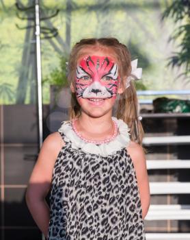 Little girl stands with face painted as a cat