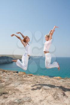 Two jumping women in white cloth against the sea
