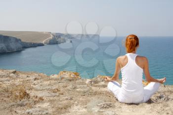 Woman in white meditating in mountains against the sea