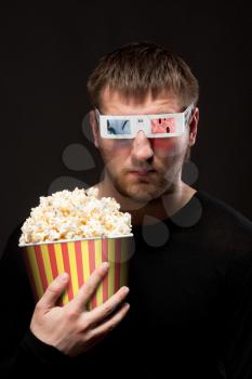 Portrait of serious man watching 3D movie and holding bucket of popcorn
