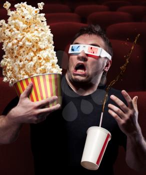 Portrait of very scared man watching 3D movie, drinking cola and eating popcorn