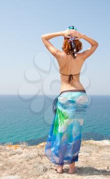 Woman in bikini and sarong on the beach looking at the sea