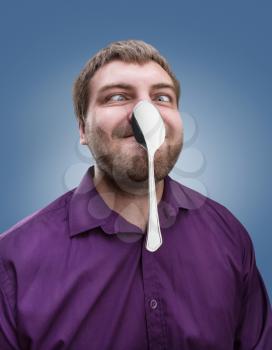 Strange adult man holds a spoon on his nose 