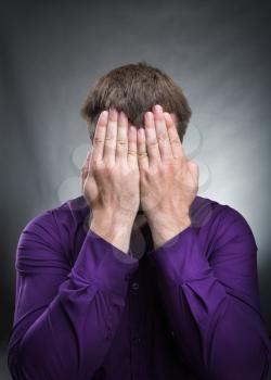 Man covers his face with hands over grey background