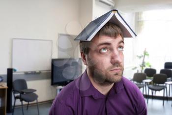 Exhausted businessman with notebook on his head in the room