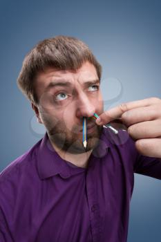 Strange bearded man with pencil in the nose over blue