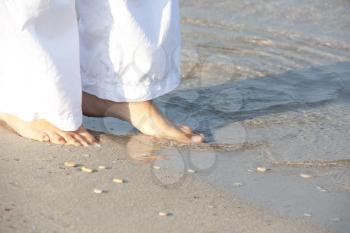 Woman in white walking barefoot on the beach