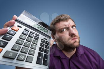 Upset man holds calculator with a big total over grey