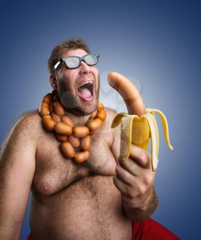 Mad man in glasses with sausages round his neck holds a big wurst in bananas peel over blue