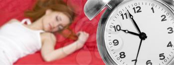 Alarm clock and sleeping young woman on background