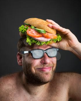 Happy man in glasses holding sandwich on his head over dark background