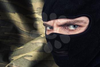 Serious man in a balaclava mask against military camouflage background