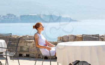 Woman is sitting infront sea view terrace of the luxury hotel of Montenegro with mountain view