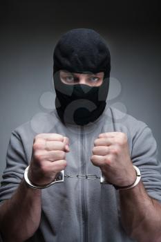 Criminal in black mask with handcuffs over grey