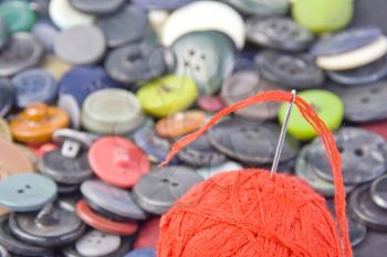 Sewing needle in ball of threads with buttons on background