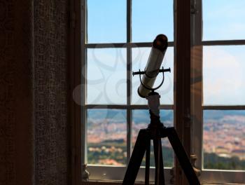 Silhouette of telescope stands in the room near the window