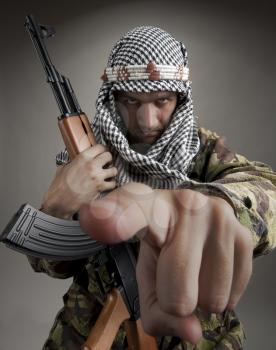 Serious middle eastern man with AK-47 pointing to you