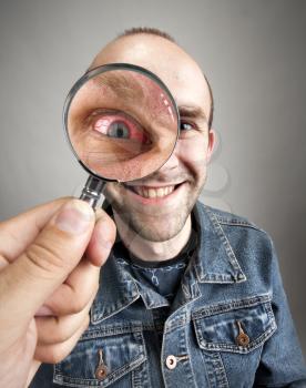 Looking to funny smiling man with angry eye through magnifying lens